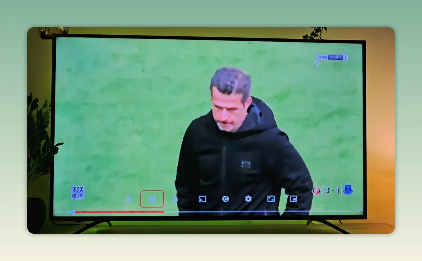 Live sports stream playing on the TV with an on screen player control bar and a football coach visible on the field